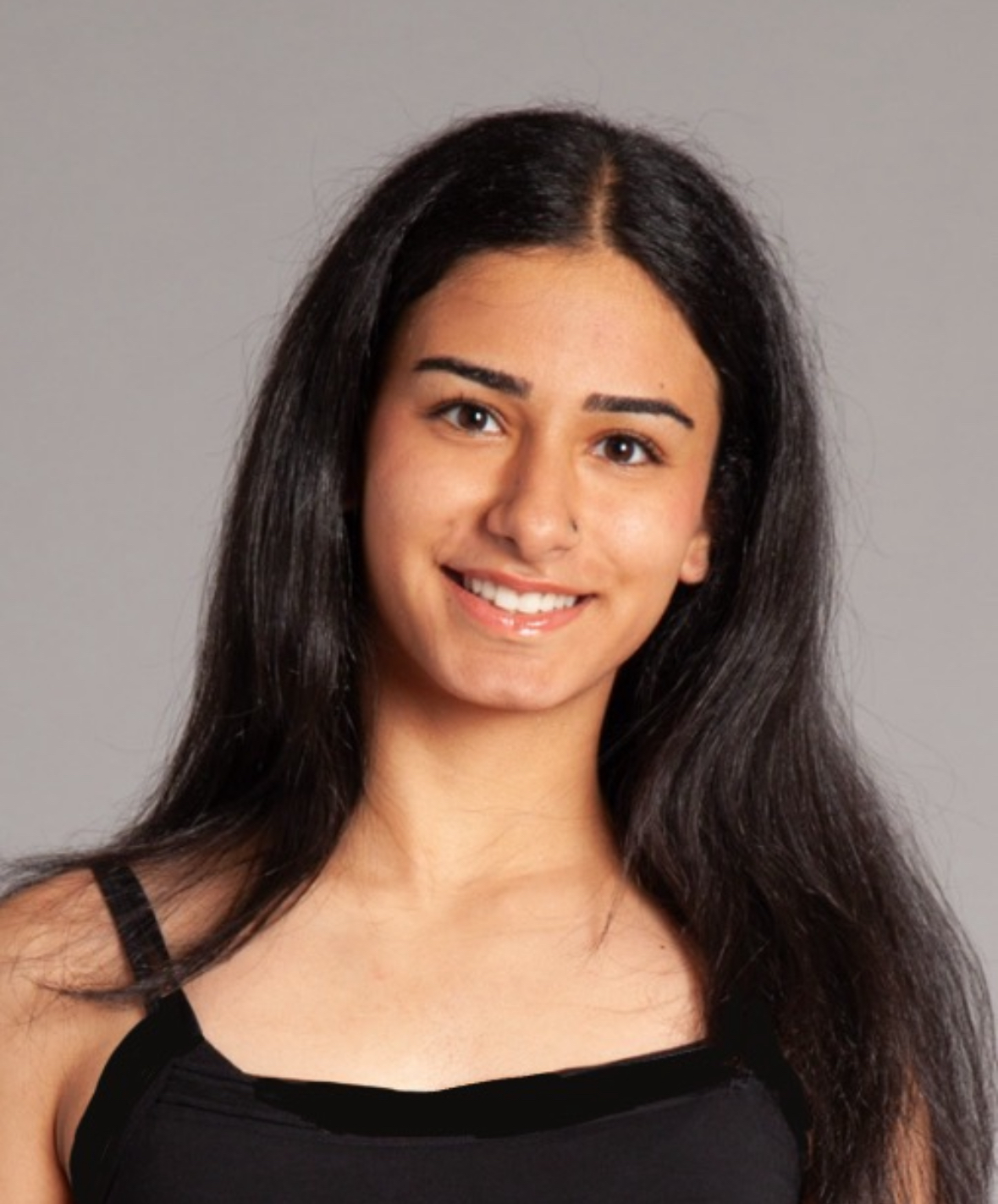 Delnaz is looking directly at the camera and smiling. She has black hair and is wearing a black top